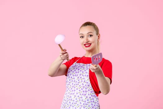 front view young pretty housewife in cape with spoons on pink background uniform duty job profession cooking worker horizontal occupation