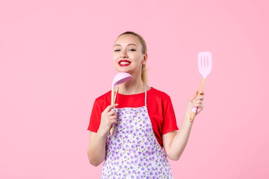 front view young pretty housewife in cape with spoons on pink background uniform duty job profession cooking worker wife horizontal