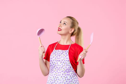 front view young pretty housewife in cape with spoons on pink background uniform job profession cooking worker wife duty horizontal occupation