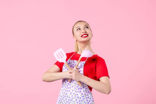 front view young pretty housewife in cape with spoons on pink background uniform job profession cooking worker wife horizontal occupation