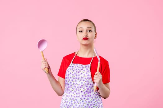 front view young pretty housewife in cape with spoons on pink background uniform profession horizontal cooking job wife duty occupation