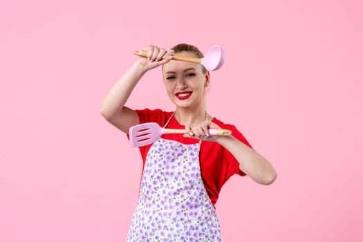 front view young pretty housewife in cape with spoons on pink background uniform profession horizontal cooking worker job wife duty