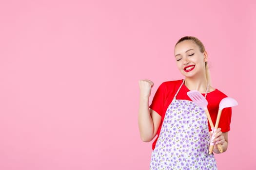 front view young housewife in cape holding spoons on pink background horizontal profession occupation duty job worker wife cutlery