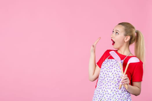 front view young housewife in cape holding spoons on pink background horizontal profession occupation duty job worker wife uniform