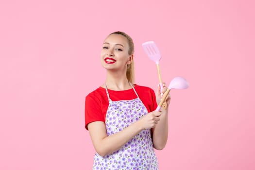 front view young housewife in cape holding spoons on pink background horizontal uniform duty occupation profession cutlery job worker