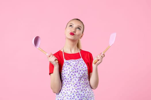 front view young housewife in cape holding spoons on pink background horizontal uniform duty profession cutlery job wife worker occupation