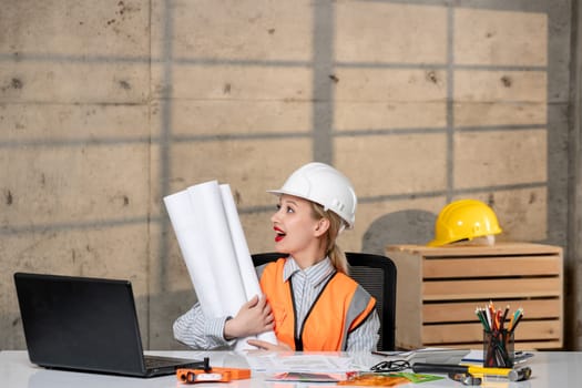 engineer blonde young cute smart girl civil worker in helmet and vest with paper rolls