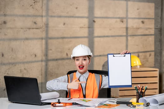 engineer cute young blonde smart girl civil worker in helmet and vest excited about plan