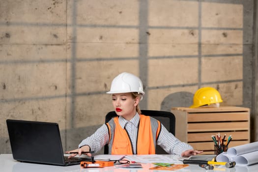engineer cute young blonde smart girl civil worker in helmet and vest working typing
