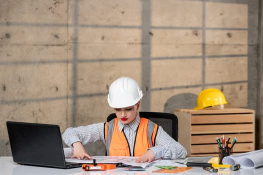 engineer smart young cute blonde girl civil worker in helmet and vest drawing plan