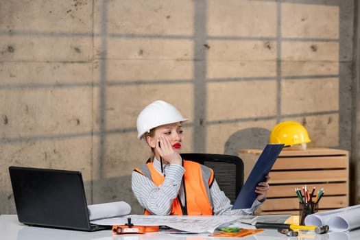 engineer smart young cute blonde girl civil worker in helmet and vest looking at project of home