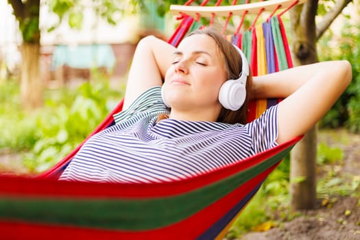 Young woman in headphones listening to music while resting in hammock outdoors.