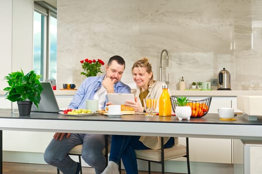 Young beautiful caucasian couple sitting at table while having breakfast at home Happy couple having breakfast together before leaving to work