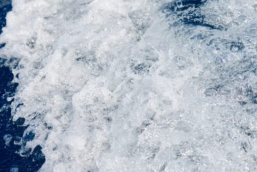 Abstract blue sea water with white waves. Blue sea texture with waves and foam. Rough deep turquoise and blue Mediterranean sea. Sea water top view.