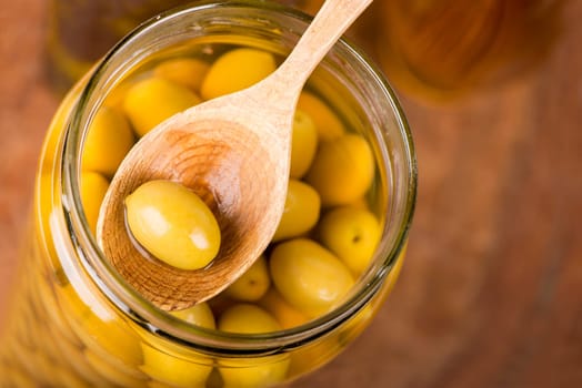 Close up green olives in bank, rosemary on a wooden background