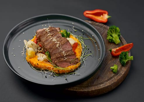 A deliciously appetizing pumpkin puree with chunks of beef meat with spices and herbs in a green plate on a dark table.