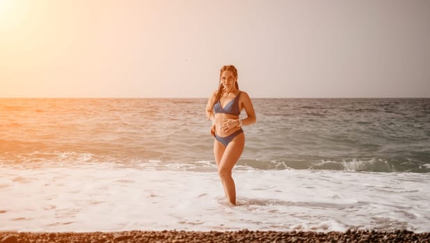 Beach vacation. Hot beautiful woman in sunhat and bikini standing with her arms raised to her head enjoying looking view of beach ocean on hot summer day.