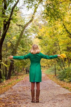 Woman with her arms outstretched holding fall leaves and enjoys in autumn.