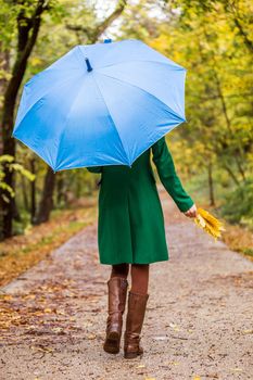 Woman holding umbrella and fall leaves while walking in the park.