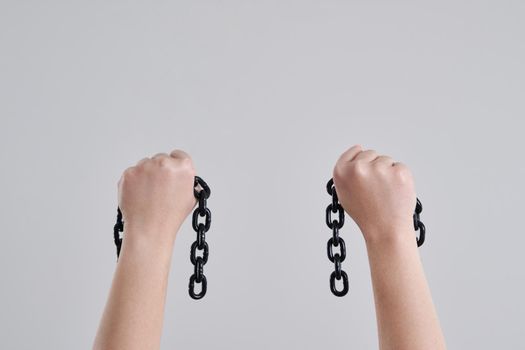 Female hands holding a broken metal chain over grey background