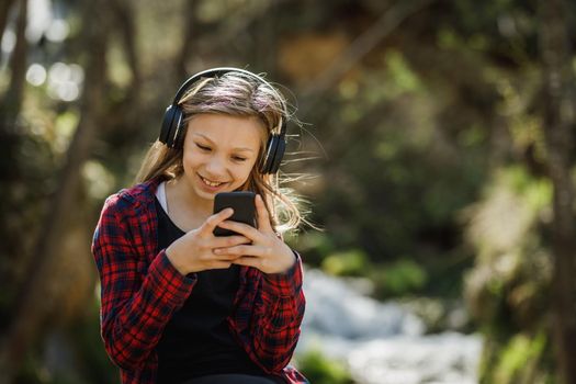 A smiling teenager girl using her smartphone while listening music in nature.
