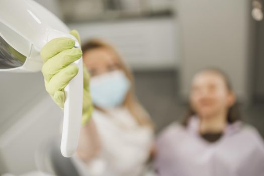 Close-up of an unrecognisable dentist holding dental lamp while having a consultation with patient in an office .