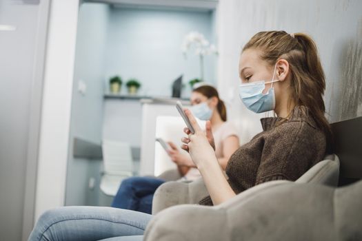 A cute teenager girl wearing face mask and using her cellphone in waiting room at dentist's office.