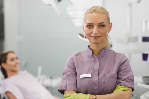 Portrait of a smiling female dentist standing with her arms folded while looking at the camera in her office.