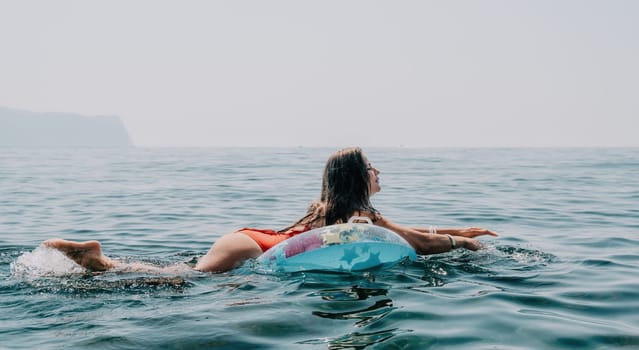 Woman summer sea. Happy woman swimming with inflatable donut on the beach in summer sunny day, surrounded by volcanic mountains. Summer vacation concept