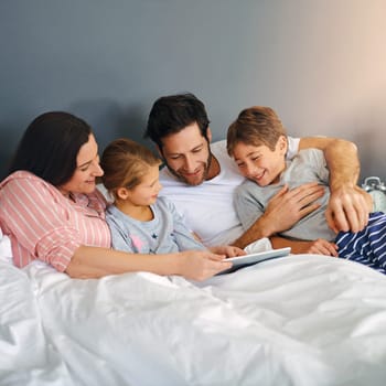 Spending time together, any opportunity we get. a young family using a tablet while chilling in bed together at home