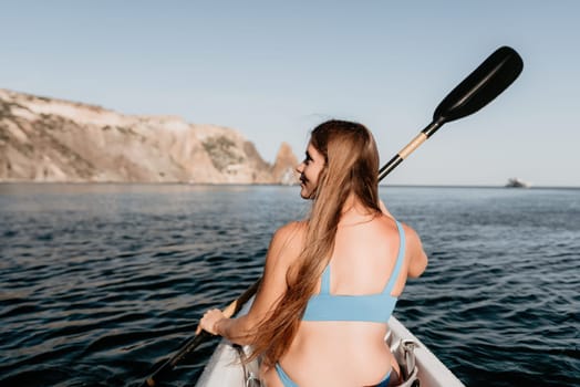 Woman in kayak back view. Happy young woman with long hair floating in transparent kayak on the crystal clear sea. Summer holiday vacation and cheerful female people relaxing having fun on the boat