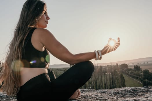 Well looking middle aged woman with long hair, fitness instructor in leggings and tops doing stretching and pilates on the rock near forest. Female fitness yoga routine concept. Healthy lifestyle.