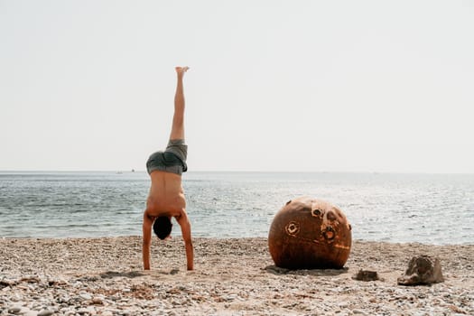 Man doing yoga poses standing on old rusty floating marine mine on the beach with rocky shore and sea background