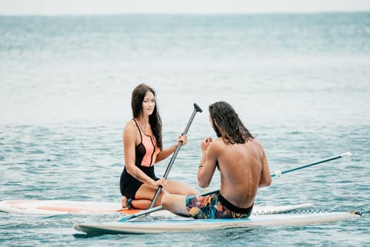 Sea woman and man on sup. Silhouette of happy young woman and man, surfing on SUP board, confident paddling through water surface. Idyllic sunset. Active lifestyle at sea or river