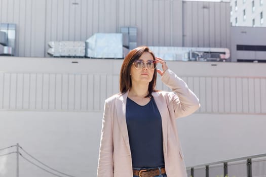 Portrait Confident Mature 40 yo Business Woman, Manager. Industrial Construction, Factory on Background. Caucasian Burnette Female In Sunglasses Looks Away, Wears Pink Jacket, Blue Shirt. Horizontal