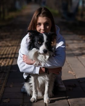 Caucasian woman hugging border collie in autumn park. Portrait of a girl with a dog