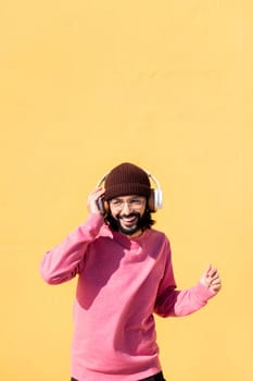 man dancing happy listening to music in his headphones with a yellow wall in the background, concept of rhythm and positive people, copy space for text