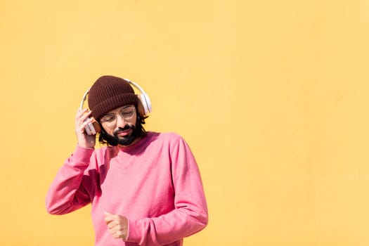 man dancing happy listening to music in his headphones with a yellow wall in the background, concept of rhythm and positive people, copy space for text