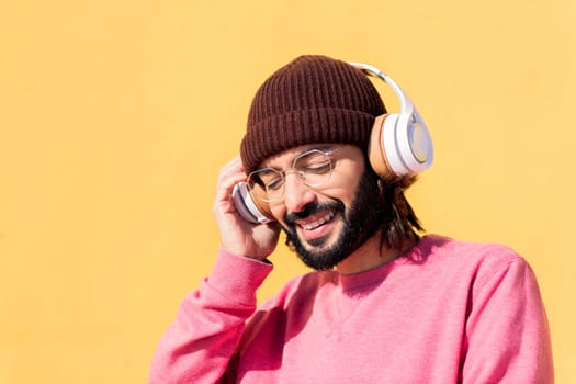 man with a pink jumper enjoying happy the music in his headphones with a yellow wall in the background, concept of rhythm and positive people, copy space for text