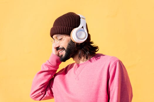young man enjoying happy the music in his headphones with a yellow wall in the background, concept of rhythm and positive people, copy space for text