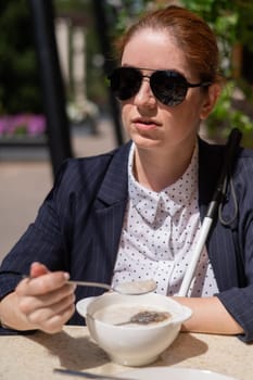 Blind caucasian woman in suit eating porridge for breakfast in outdoor cafe