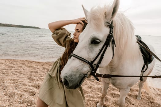 A woman in a dress stands next to a white horse on a beach, with the blue sky and sea in the background