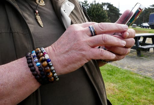Hands of a fashionable man with ring and bracelets, using his smartphone