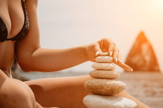 Woman bilds stones pyramid on the seashore on a sunny day on the blue sea background. Happy holidays. Pebble beach, calm sea, travel destination. Concept of happy vacation on the sea, meditation, spa