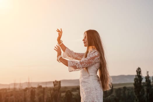 Romantic beautiful bride in white dress posing with sea and mountains in background. Stylish bride standing back on beautiful landscape of sea and mountains on sunset