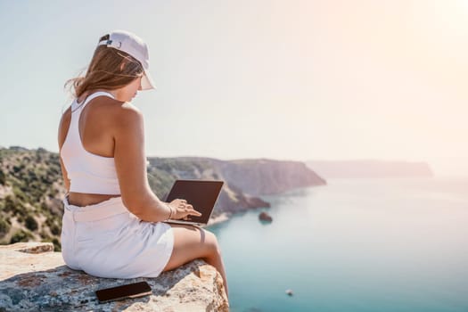 Digital nomad, Business woman working on laptop by the sea. Pretty lady typing on computer by the sea at sunset, makes a business transaction online from a distance. Freelance remote work on vacation