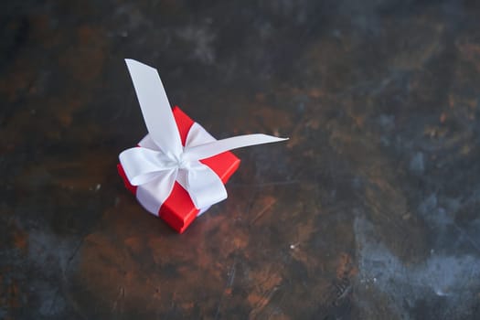 Small red gift box with a white bow on dark background. High-quality photo. Copy space.