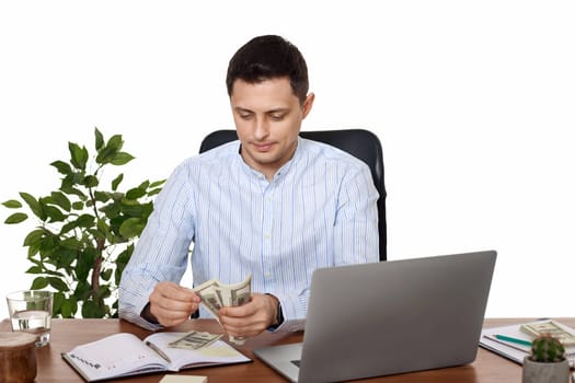young handsome businessman working on laptop and holding money while sitting on chair at desk.