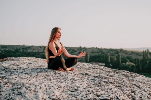 Well looking middle aged woman with long hair, fitness instructor in leggings and tops doing stretching and pilates on the rock near forest. Female fitness yoga routine concept. Healthy lifestyle.