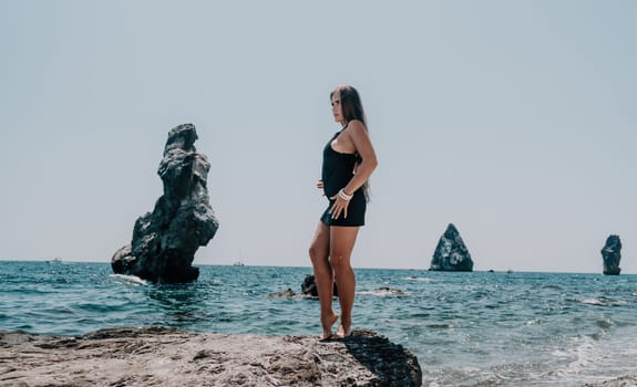 Woman travel sea. Young Happy woman in a long red dress posing on a beach near the sea on background of volcanic rocks, like in Iceland, sharing travel adventure journey